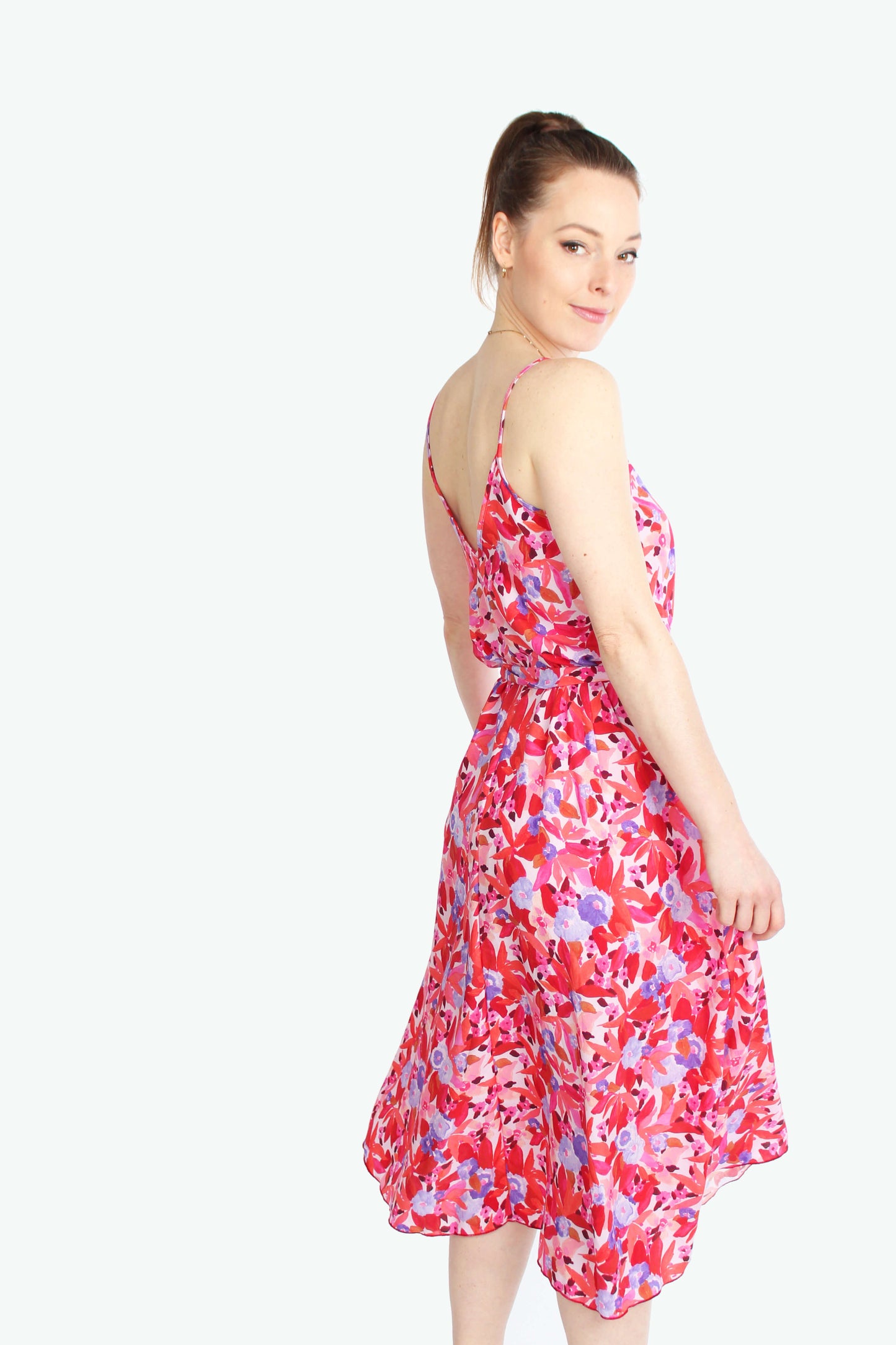 Frau, schaut über die Schulter in einem schwingenden Sommerkleid in Midilänge in rot/rosé geblümt mit Spaghettiträgern aus leichtem Viskosestoff von LA.LUKA Berlin.